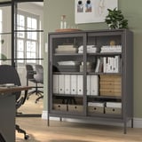 Armoire de rangement noire IDÅSEN avec portes vitrées dans le bureau, contenant des livres et des objets de décoration, économise de l’espace.