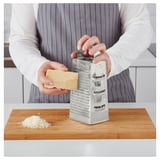 La personne râpe le fromage à l’aide d’une râpe en acier inoxydable à deux côtés sur une planche à découper en bois.