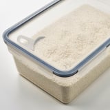 Récipient en plastique transparent avec couvercle bleu, contenant des grains blancs, probablement du riz, contenu facile à voir et à accéder, empilable pour un stockage peu encombrant.