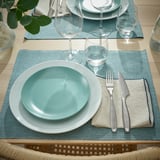 Table dressée avec des assiettes, des verres et des couverts bleu-vert. Fourchette et couteau soigneusement disposés avec une serviette à côté, prêts pour le dîner.