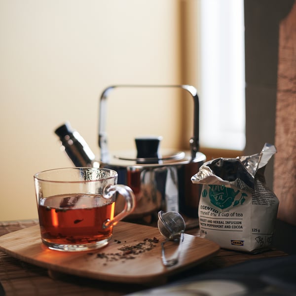 Tasse en verre transparent sur un plateau en bois, avec théière en argent et sachet de thé, montrant une facilité à voir la force du thé.