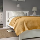 Lit avec une pâte à tartiner en coton INDIRA jaune moutarde, des oreillers à motifs, une table de chevet, une lampe et des pantoufles, créant une configuration confortable et élégante.