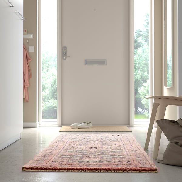 Une entrée minimaliste avec un tapis coloré, des baskets blanches et une chaise près d’une porte.