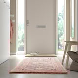 Une entrée minimaliste avec un tapis coloré, des baskets blanches et une chaise près d’une porte.