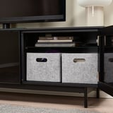 Meuble TV noir avec portes ouvertes, boîtes de rangement en feutre gris, livres et une lampe.