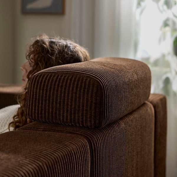 Gros plan : personne allongée sur un canapé marron JÄTTEBO , mettant en valeur son appuie-tête moelleux et confortable.