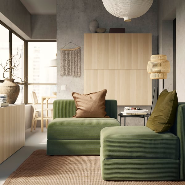Salon moderne avec canapé JÄTTEBO vert, armoire en bois et lampe tressée.