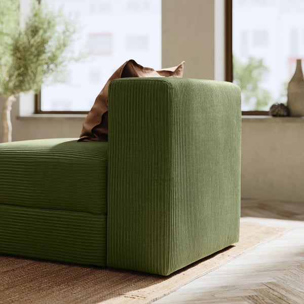 Canapé vert confortable en forme de L avec de grands coussins et une couverture. Parfait pour se détendre et socialiser.