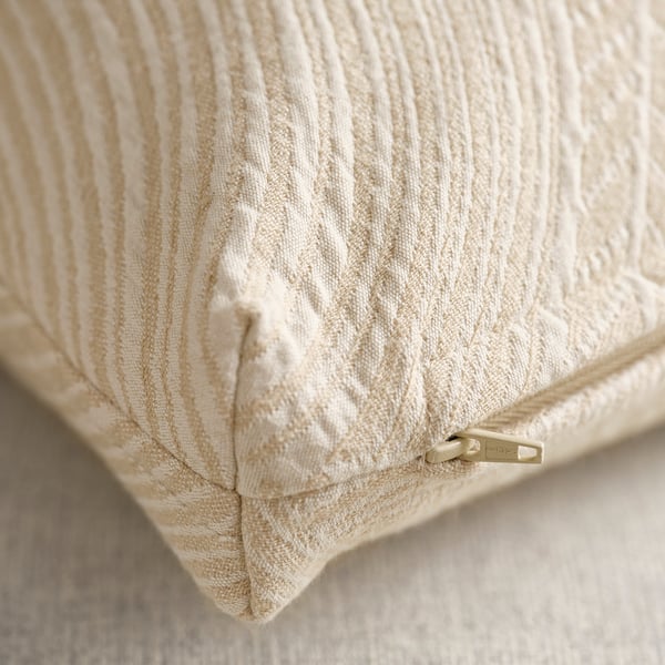 Gros plan d’un coussin texturé blanc cassé avec fermeture éclair, présentant un motif en forme de feuille.