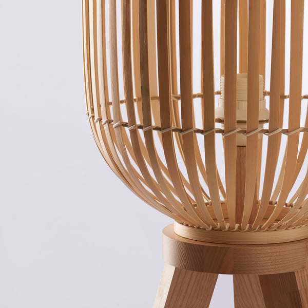 Lampe en bambou fabriquée à la main sur un support en bois, émettant une lumière douce et chaude.