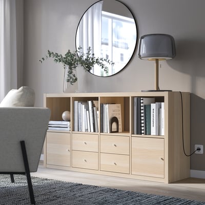 Enfilade KALLAX avec étagères et tiroirs, miroir et lampe, quelques livres et un vase.