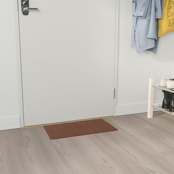 Petit paillasson brun rectangulaire à côté d’une porte blanche, s’insérant parfaitement dans l’espace.