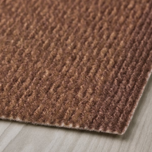 Paillasson brun à surface texturée, probablement en polyester recyclé, montré sur une surface plane. Le matériau semble durable et facile à nettoyer.