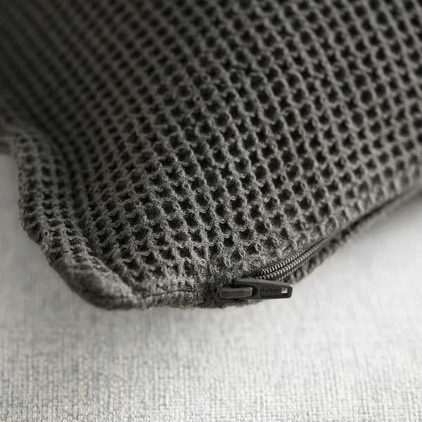 Housse de coussin noire avec un motif en maille texturée, détail de fermeture éclair, reposant sur une surface légère.