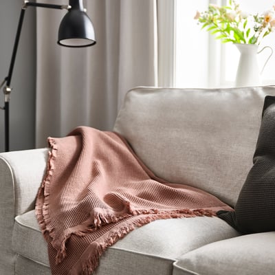 Salon moderne avec canapé gris, couverture, lampe et fleurs.