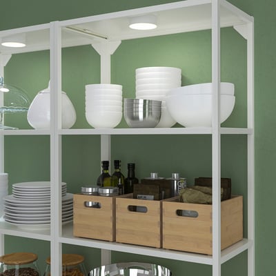 Étagère blanche avec bols, boîtes et verres. La lumière supérieure illumine l’étagère.