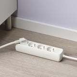 Rallonge blanche avec 3 prises sur parquet, offrant des prises supplémentaires.