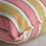 Gros plan d’une housse de coussin pliée à rayures horizontales beige, rouge clair et blanc, avec une fermeture éclair cachée.