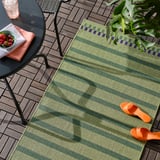 Patio extérieur avec tapis vert KORSNING, toboggans orange, plante et table avec des fruits.