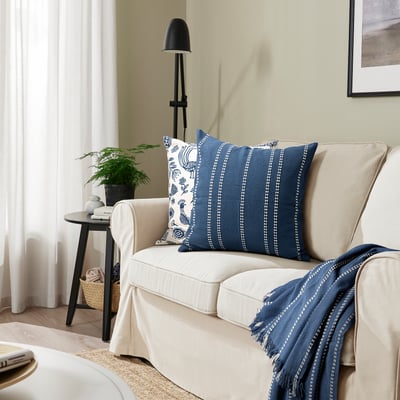 Canapé beige avec coussin KRUTBRÄNNARE à rayures bleues.