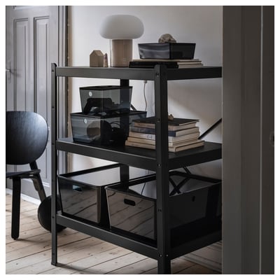 Étagère en métal noir avec divers articles, notamment une lampe, des boîtes et des livres. Design moderne et minimaliste.
