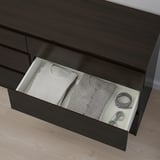 Commode sombre ouverte avec des vêtements et des accessoires soigneusement pliés dans un tiroir blanc.