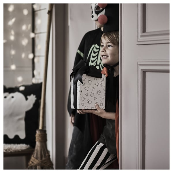 Jeune garçon en costume d’Halloween tenant une boîte emballée dans un emballage cadeau, peut-être pour la chasse aux bonbons.