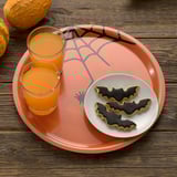 Plateau sur le thème d’Halloween avec du jus d’orange et des biscuits de chauve-souris. Le plateau a des bords inclinés pour un transport facile.