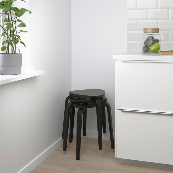Petit tabouret noir à trois pieds placé dans la cuisine moderne, à côté d’une armoire blanche.