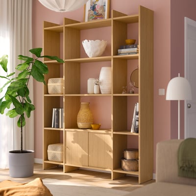 Étagère en bois LÅDMAKARE en chêne clair, avec rangement ouvert et fermé, contenant des livres, des vases et des plantes, haute contre un mur rose.