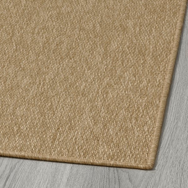 Tapis d’extérieur doux et beige avec tissage détaillé, exposé sur un plancher en bois.