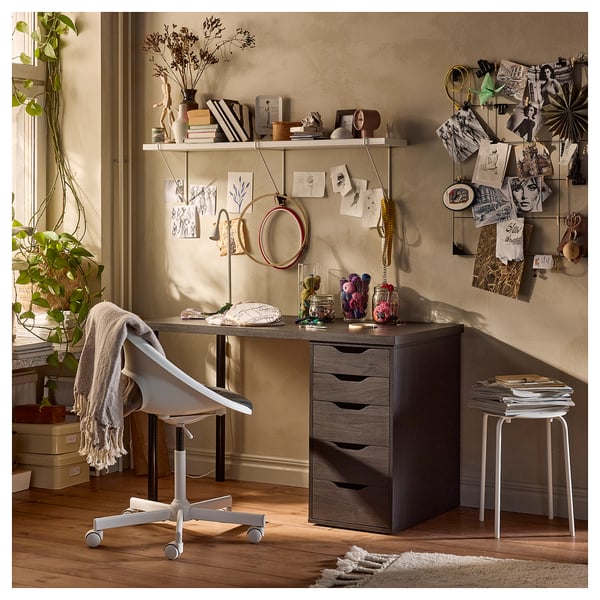 Bureau à domicile confortable avec bureau LAGKAPTEN en bois sombre, chaise blanche et étagères décorées.