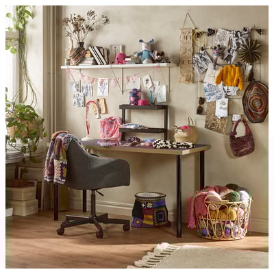 Bureau d’artisanat confortable avec fil, projets et décoration ; bureau LAGKAPTEN noir et chaise grise.