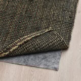 Tapis en jute vert foncé sur parquet, sous-couche grise, tissé à plat pour faciliter l’entretien et le chauffage.