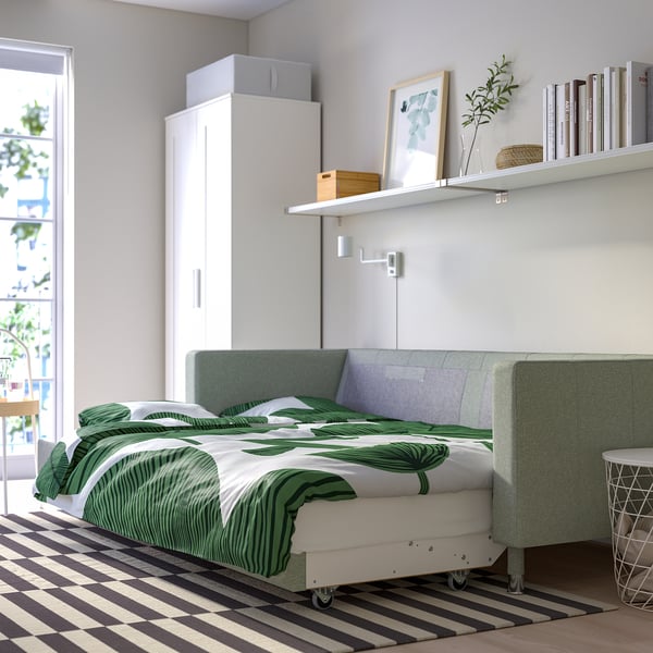 Canapé-lit moderne avec pieds chromés ; se transforme en zone de sommeil ; stocke le linge à l’intérieur ; Imprimé feuille tropicale vert clair.