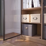 L’armoire à portes vitrées présente des livres et des boîtes, avec des poignées en métal et des étagères en bois, fixées au mur.