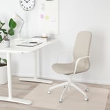 Chaise de bureau LÅNGFJÄLL blanche avec hauteur réglable et roulettes à côté d’un bureau avec des éléments de bureau essentiels comme une lampe, une plante et un calendrier.