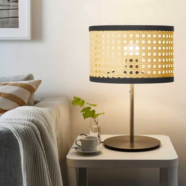 Lampe en osier teinté or sur socle en laiton à côté d’un canapé beige.