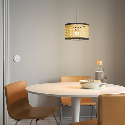 Lampe suspendue LÅNGSKEPPS au design en osier, qui brille chaleureusement au-dessus de la table à manger.