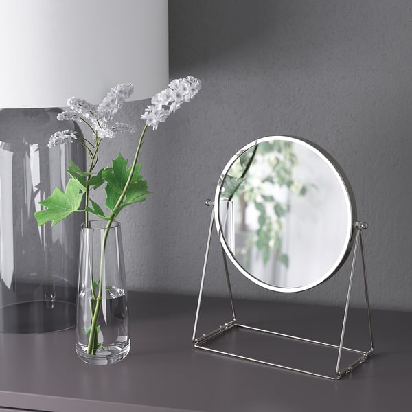 Vase en verre avec des fleurs blanches à côté du miroir LASSBYN.