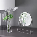 Vase en verre avec des fleurs blanches à côté du miroir LASSBYN.