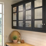 Cuisine moderne avec armoires noires, vaisselle, comptoir en bois et plateau en osier.