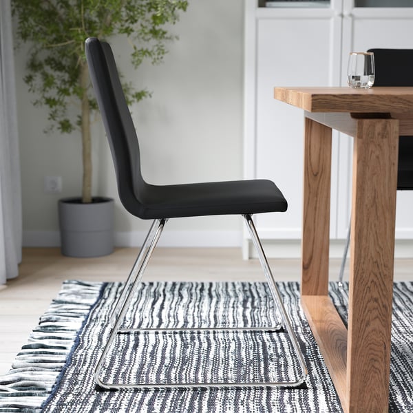 Chaise avec base luge chromée, assise et dossier rembourrés, sur tapis à motifs à côté d’une table en bois avec verre.