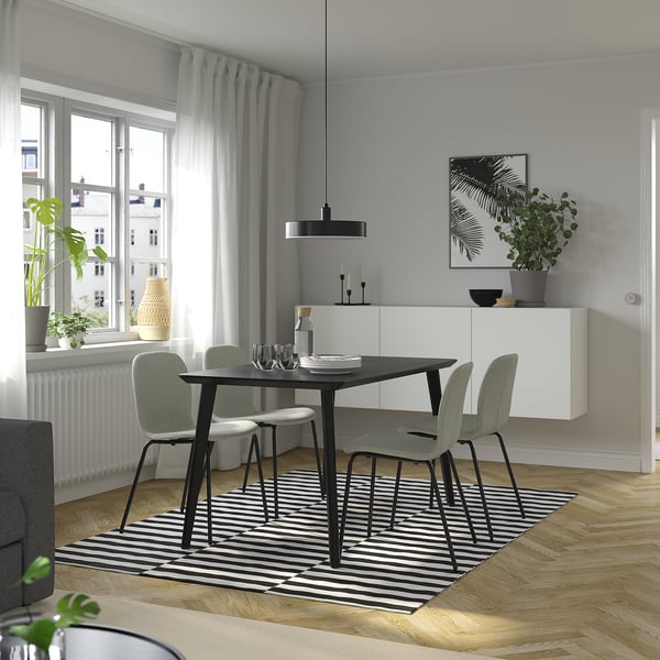 Salle à manger moderne avec ensemble 4 places LISABO, table noire, chaises grises, tapis rayé et œuvres d’art.