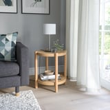 Table d’appoint ronde en bois LISTERBY. Marron clair, design simple, à côté de la chaise grise et de la lampe blanche.