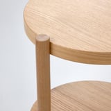 Table d’appoint moderne en bois avec plateau lisse et circulaire et pied central robuste. Finition chêne naturel clair.