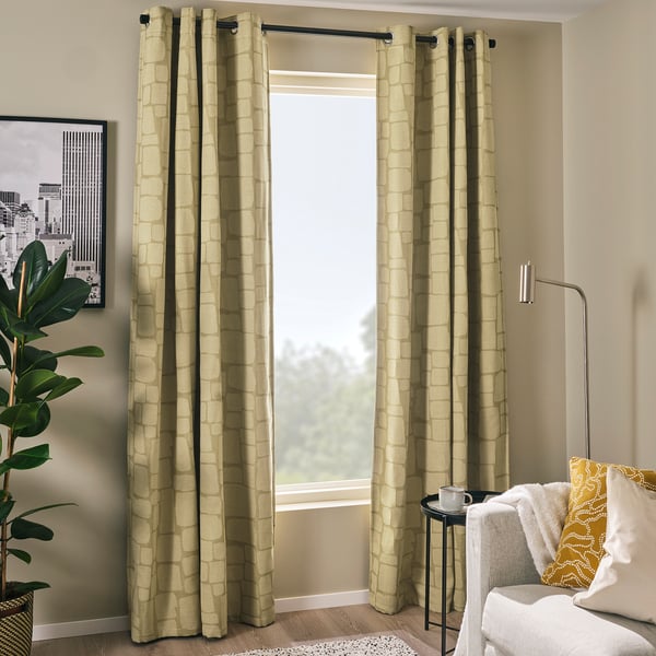 Salon moderne : les rideaux vert olive LÖNNSTÄVMAL pendent près de la fenêtre, éclairant la pièce. Plante en pot, coussin de chaux et chaise blanche à proximité.