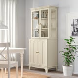 Armoire LOMMARP en bois avec portes vitrées. Grand, mettant en valeur des objets. Plante verte à côté.