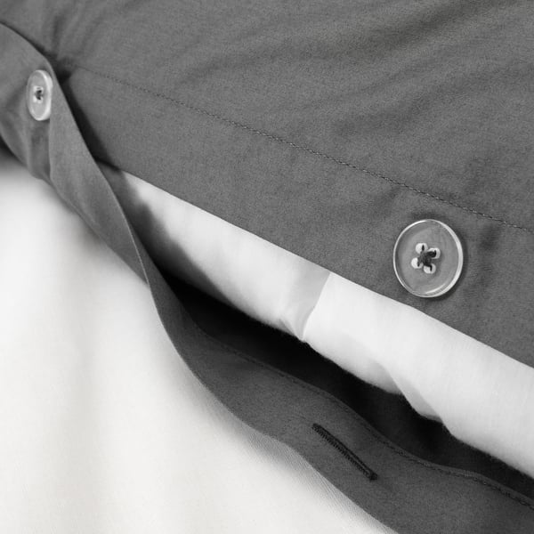 Gros plan d’une housse de couette grise avec bouton et tissu lisse, montrant des coutures fines et un tissage satiné brillant.