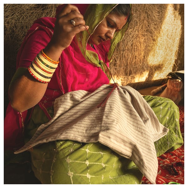 Femme en tenue traditionnelle vibrante, bijoux complexes, cousant à la main un tissu de couleur claire.